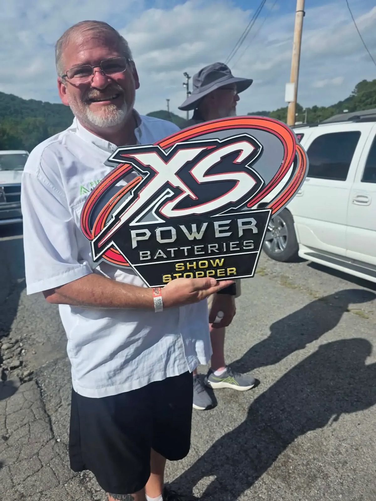 A team member in a Field Advantage shirt holding an XS Power Batteries Show Stopper award at an outdoor show.